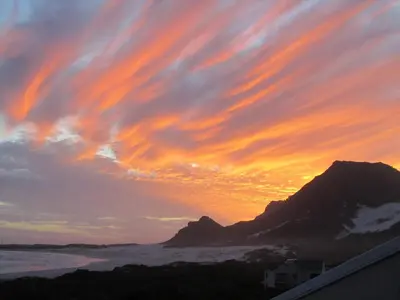a sunset over the ocean and a mountain at SeaScape Silversands in Bettyʼs Bay