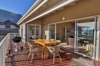 a patio with a wooden table and chairs on a deck at Tides in Bettyʼs Bay