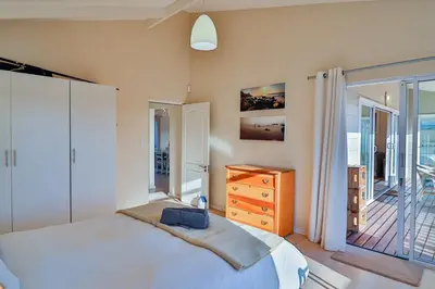 a bedroom with a bed and a dresser and a balcony at Tides in Bettyʼs Bay