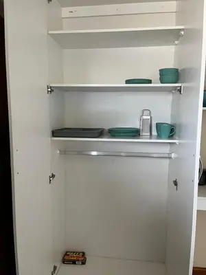 a white pantry with plates and bowls on shelves at Cute Tranquil Pool Side Apartment in Cape Town