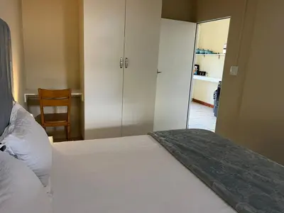 a bedroom with a white bed and a chair at Cute Tranquil Pool Side Apartment in Cape Town