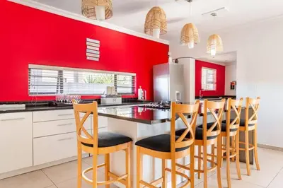 a kitchen with red walls and wooden bar stools at Spacious Room with Balcony, Mountain Views, Modern Bathroom Tub and Shower and WiFi and Pool view in Cape Town