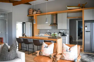 a kitchen with white cabinets and a bar with chairs at MOS- Palmiet in Kleinmond