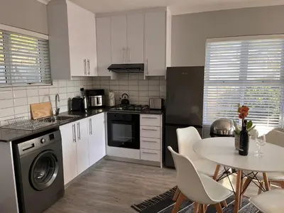 a kitchen with white cabinets and a table with chairs at Cozy Cottage in Cape Town