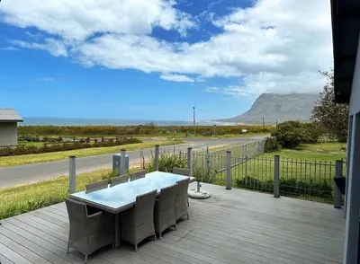 a table and chairs on a deck with a view of a road at MOS-Palmiet 72 in Kleinmond