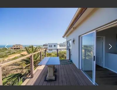 a table on a deck with a view of the beach at OceansCrest Seaview Apartment in Bettyʼs Bay