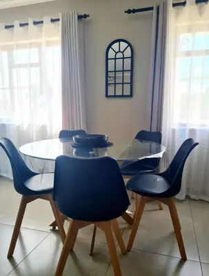 a dining room with a glass table and blue chairs at Flamingle at Coot in Cape Town