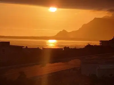 a sunset over a body of water with a mountain at La Mer in Bettyʼs Bay
