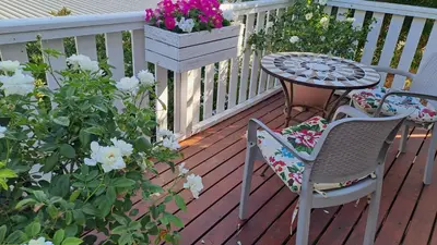 a wooden deck with a table and chairs and flowers at Martha's Place in Gordonʼs Bay