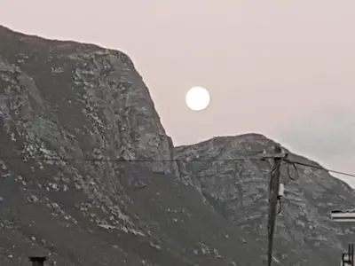 a mountain with the sun setting on top of it at Betty's Bay Quaint Cottage in Bettyʼs Bay