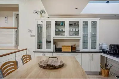 a kitchen with white cabinets and a wooden table at Onrus Beach House in Hermanus