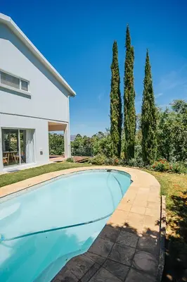 a swimming pool in front of a house with trees at On Helderberg in Somerset West
