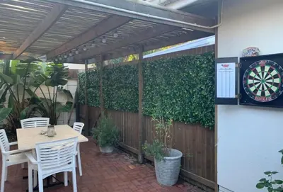 a patio with a table and a dartboard on a fence at Crinum House and cottages in Bloubergstrand in Cape Town