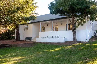 a white house with a white wall and trees at Serendipity Self-Catering Cottage in Greyton