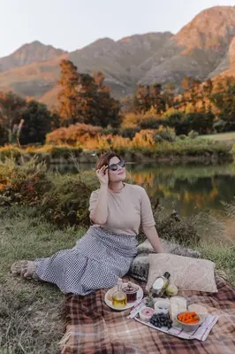 a woman sitting on a picnic blanket next to a lake at Courchevel Cottages in Franschhoek