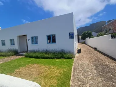 a white house with a white wall and a yard at Holiday Vibe in Hermanus
