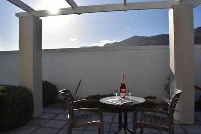 a table with a bottle of wine and chairs on a patio at PROVIDENCE VILLA -Tranquil, Neat & Private Cottage in Hermanus
