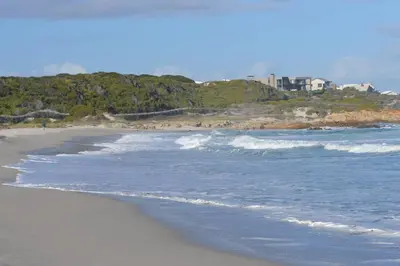 a sandy beach with waves and houses in the background at PROVIDENCE VILLA -Tranquil, Neat & Private Cottage in Hermanus