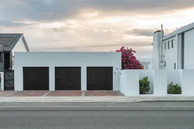 a white building with four garage doors on a street at Fun in the Voelklip Sun in Hermanus