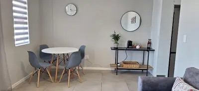 a living room with a table and chairs and a clock at Sound of the surf in Cape Town