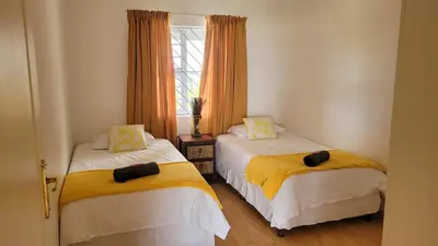 a bedroom with two beds with yellow and white sheets at Judea Accommodation in Bettyʼs Bay