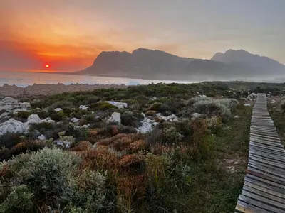 a sunset over the ocean with a wooden boardwalk at La Mer Seafront Selfcatering Accommodation Kleinmond in Kleinmond