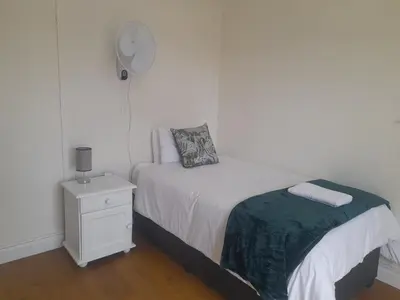 a white bedroom with a bed and a night stand at Cornerstone Guesthouse Drostdy in Panorama
