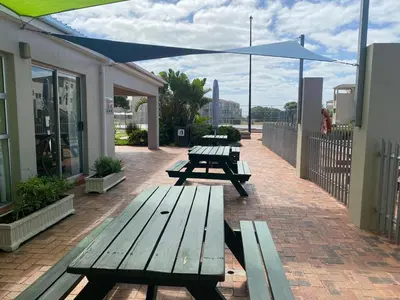 two picnic tables on a brick patio with an umbrella at Oceanfront Escape with Spacious Balcony Hermanus in Hermanus