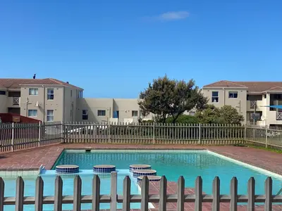 a swimming pool with two chairs and a fence at Oceanfront Escape with Spacious Balcony Hermanus in Hermanus