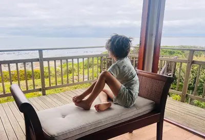 a young girl sitting on a chair on a porch looking at the ocean at Unique views Betties Bay in Bettyʼs Bay