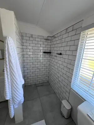 a white tiled bathroom with a shower and a window at Unique views Betties Bay in Bettyʼs Bay