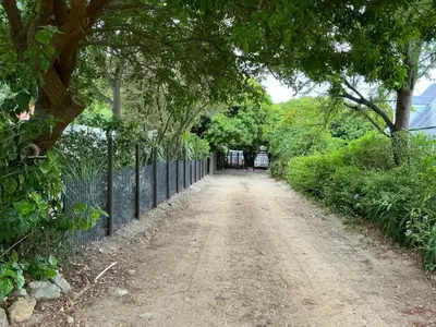 a dirt road with a fence and trees at Swallows Cottages in Hermanus