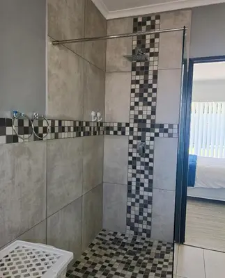 a shower with a glass door in a bathroom at Frangipani House in Goodwood