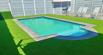 a swimming pool with grass and chairs in a yard at Frangipani House in Goodwood