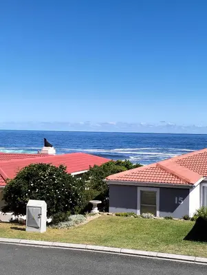 a house with red roofs next to the ocean at Hermanus Beach Club 223 in Hermanus