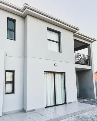a white house with black windows and a balcony at Goodness Century Apartment in Cape Town