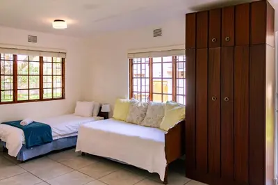 a room with two beds and a cabinet and windows at Mountainside Beach House in Hermanus