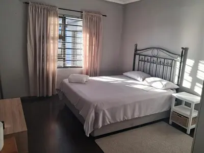 a bedroom with a bed with white sheets and a window at Spacious Home-Quiet area, Kuils river, Cape Town in Blackheath