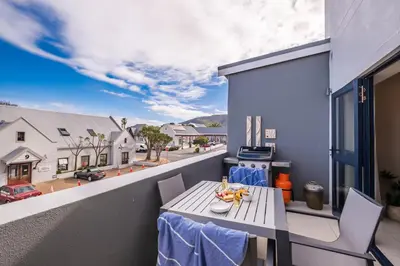 a balcony with a table and chairs and a street at Hermanus Marine Square spacious 1 bedroom- central & close to sea in Hermanus