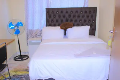 a bedroom with a white bed with a headboard and a fan at Kitty Guest House in Bellville
