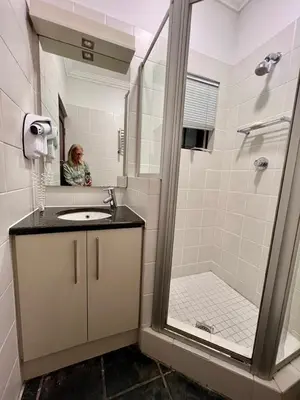 a woman in a bathroom with a sink and a shower at Studio 5 at Huis Piron in Stellenbosch
