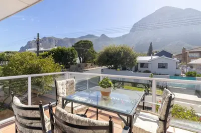 a glass table and chairs on a balcony with mountains at Vonkelwyn - enjoy Grotto Beach sunsets in Hermanus