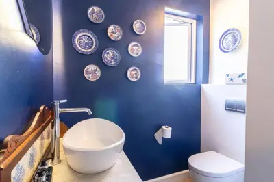 a bathroom with a blue wall with a sink and a toilet at Vonkelwyn - enjoy Grotto Beach sunsets in Hermanus