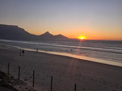 a sunset on the beach with people walking on the beach at Sunset at Keys in Cape Town