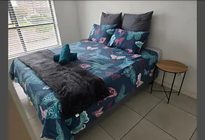 a bed with a blue comforter and a table at Sunset at Keys in Cape Town