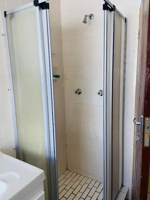a shower with a glass door next to a sink at GWMV Guest House in Cape Town
