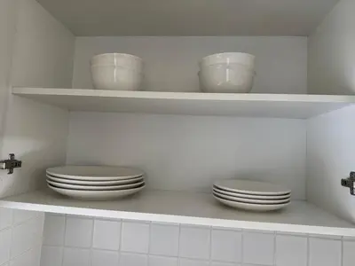 a white kitchen with plates and bowls on shelves at Black & White Self Catering in Paarl