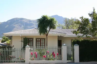 a small house with a fence and a palm tree at Cape Robin Cottage in Franschhoek