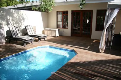 a swimming pool on a wooden deck with two chairs at Cape Robin Cottage in Franschhoek