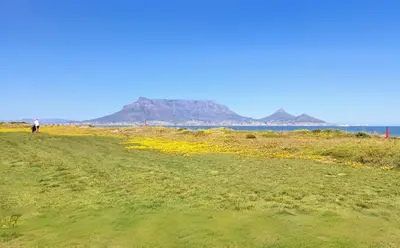 a person walking on a field with mountains in the background at Luxury Mini Villa Sunset Beach Cape Town in Cape Town